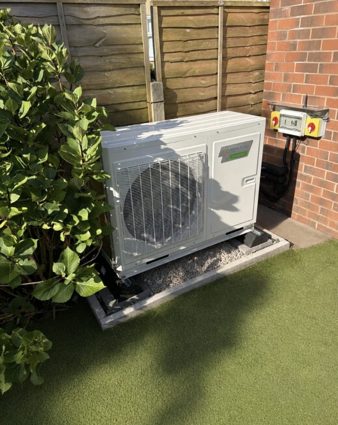 Air source heat pump installed on a gravel bed in a side return with an electrical isolator on the wall