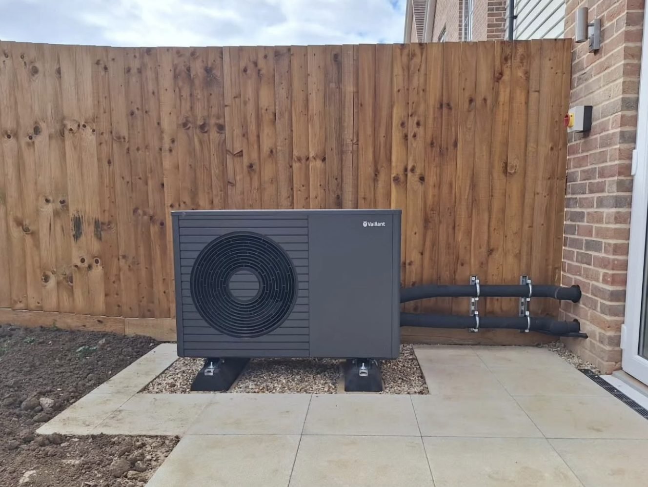 Vaillant air source heat pump installed on paving beside a new build home with lagged pipework